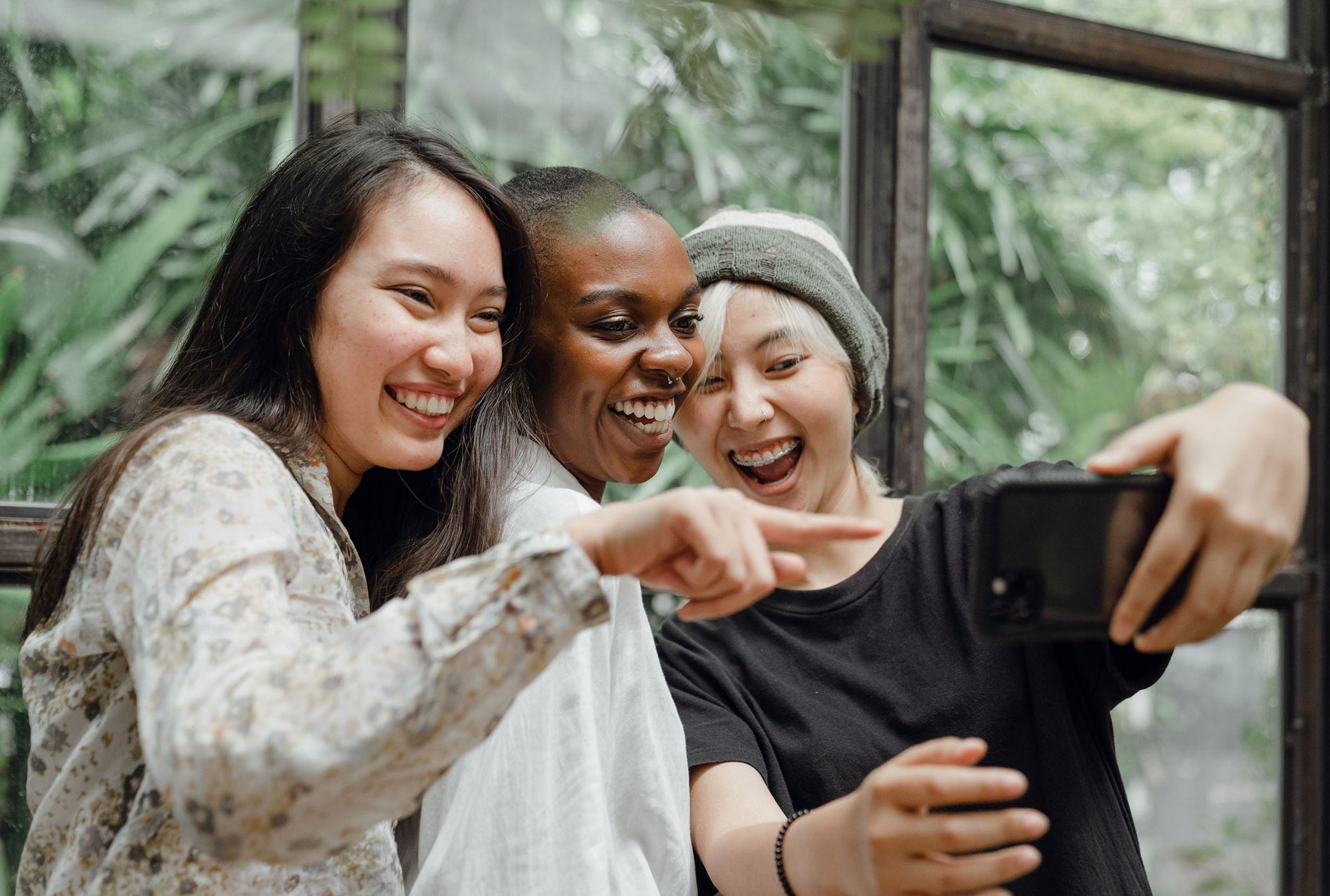 3 college students huddled together laughing at something on a phone